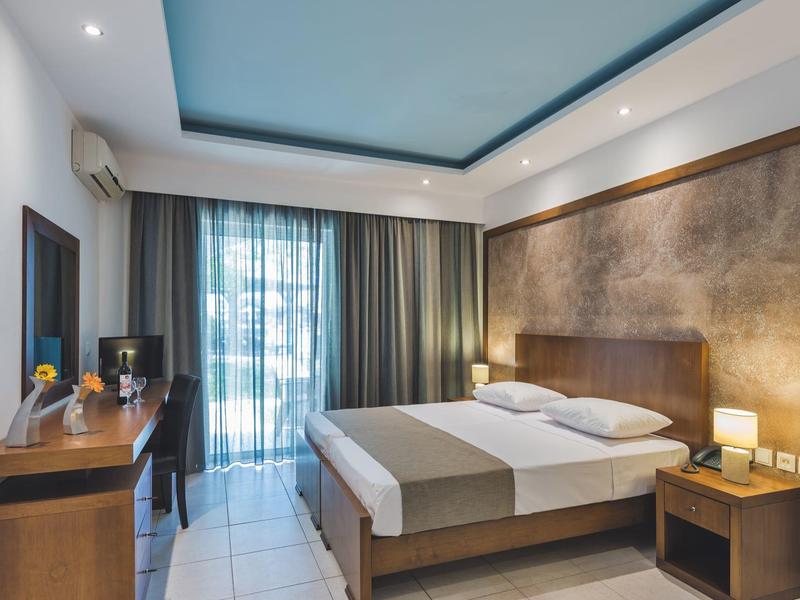 Camera d'hotel moderna con letto matrimoniale, scrivania, sedia e balcone con tende.