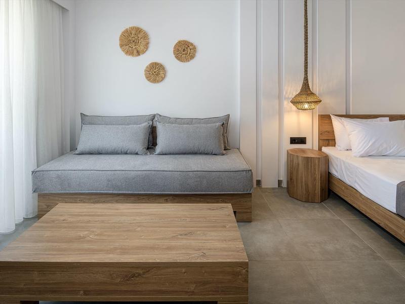 Camera d'hotel moderna con divano grigio, tavolino in legno e letto con comodino e lampada in legno.