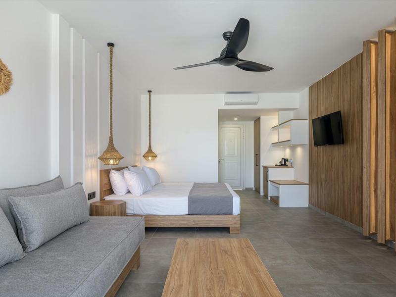 Camera d'hotel moderna con letto matrimoniale, divano, ventilatore a soffitto e dettagli in legno sulla parete.