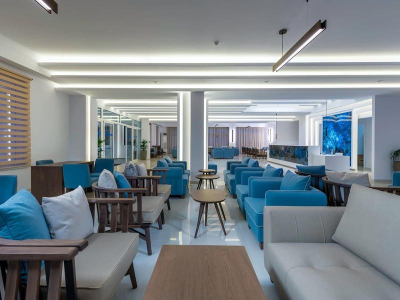 Lounge d'hotel moderno con poltrone blu, tavoli in legno e pareti chiare.