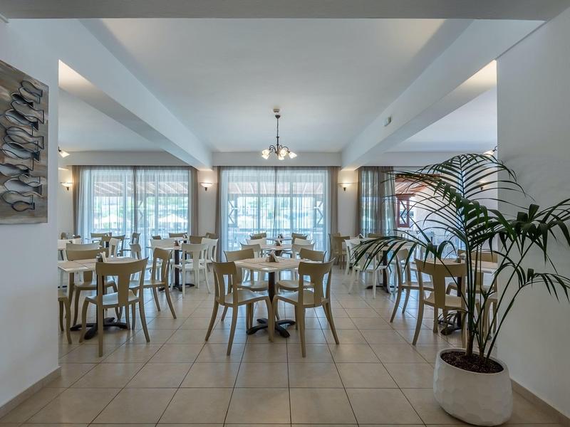 Ristorante moderno e luminoso con pareti bianche, tavoli in legno e grandi finestre.