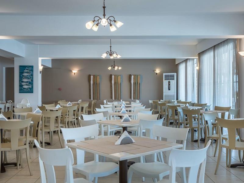 Grande sala da pranzo luminosa con molte sedie e tavoli bianchi e in legno.