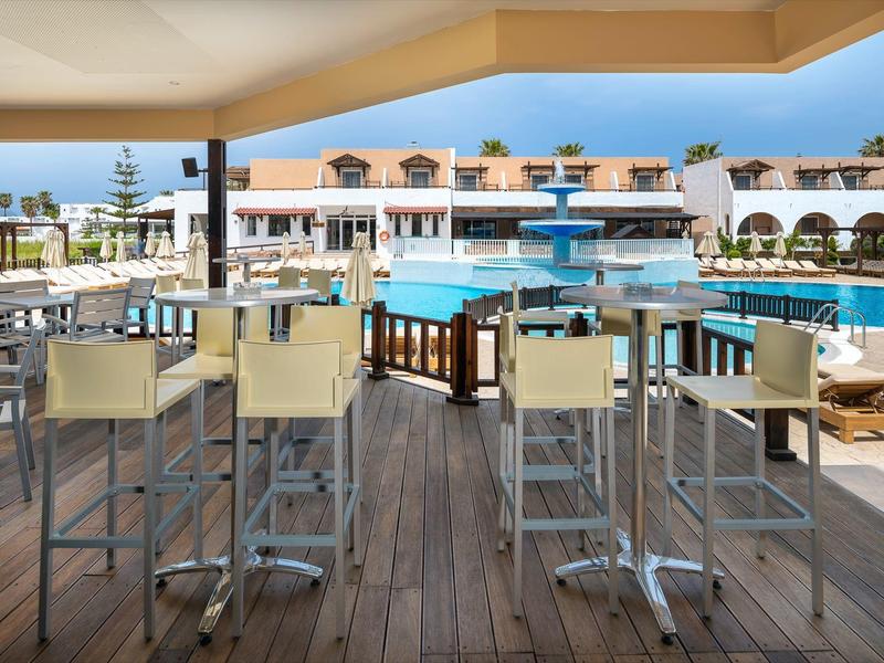 Vista di un'area piscina con sgabelli da bar e tavoli sotto una zona coperta in un hotel.