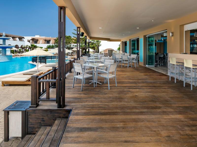 Terrazza con tavoli e sedie accanto alla piscina di un hotel in una giornata di sole.