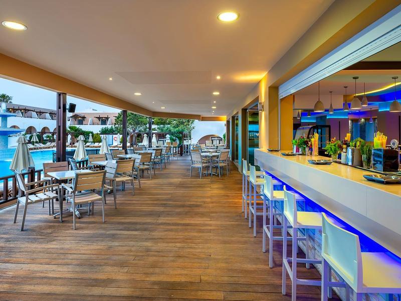 Area bar moderna dell'hotel con bancone e sgabelli accanto a una piscina sotto uno spazio esterno coperto.