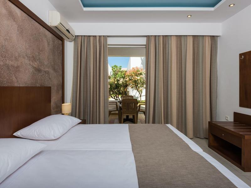 Camera d'hotel moderna con due letti, scrivania, sedia e vista su un balcone con piante.