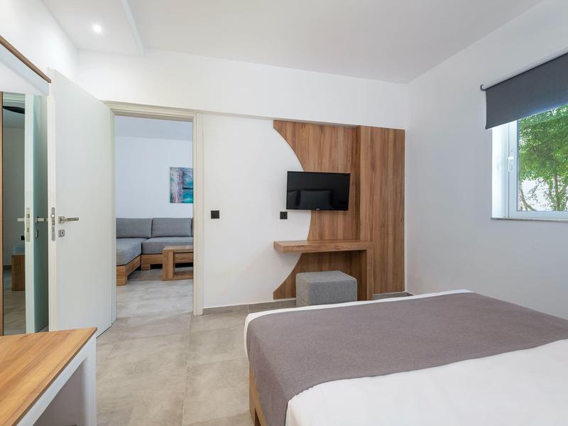 Camera d'hotel moderna con letto matrimoniale, TV e accesso a una stanza adiacente.
