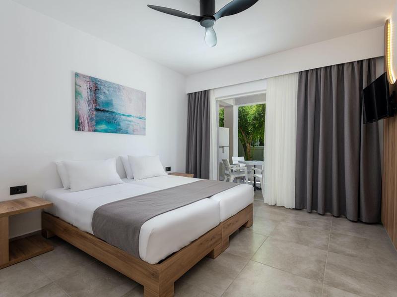 Camera d'hotel moderna con letto matrimoniale, tavolo, ventilatore a soffitto e accesso alla terrazza.