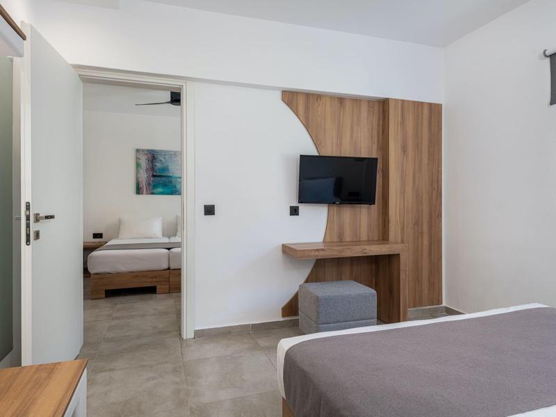 Camera d'hotel moderna con copriletto grigio, pannello in legno con TV e vista sulla camera da letto.