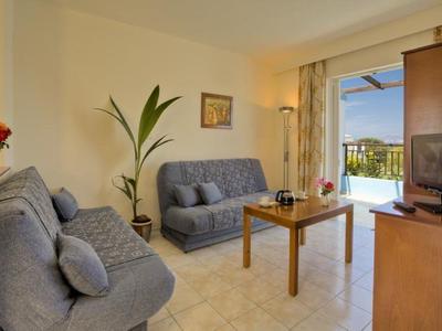 Gemütliches Wohnzimmer mit grauen Sofas, Holz-Couchtisch, Pflanze, TV und Balkon mit Meerblick.