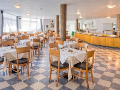 Großer, heller Speisesaal mit kariertem Boden, Holzmöbeln und gedeckten Tischen.
