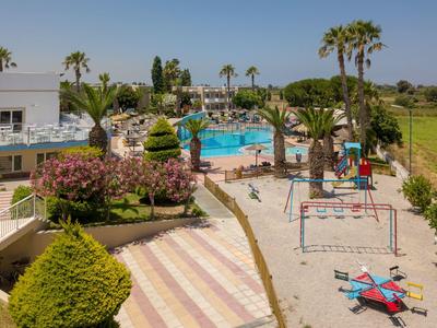Freizeitbereich mit Pool, Bäumen, Spielplatz und Sitzgelegenheiten bei sonnigem Wetter.