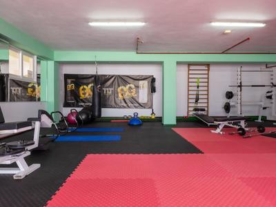 Großer Fitnessraum mit roten und blauen Matten, Kraftgeräten, Hanteln und Spiegeln an den Wänden.