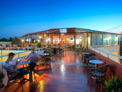 Abendliche Dachterrasse mit Sitzgelegenheiten, Beleuchtung und Gästen, klarer blauer Himmel.