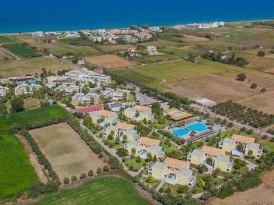 Luftaufnahme eines Ferienresorts mit gelben Gebäuden, grünem Land und blauem Pool am Meer.