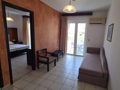 Kleines Zimmer mit roter Wand, Fliesenboden, Sofa, Tisch, Stuhl und Balkon mit Glasdrucktür.