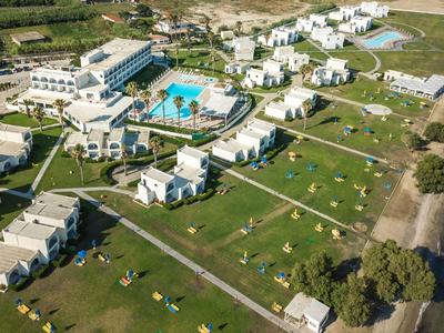 Luftaufnahme eines Strandresorts mit Gebäuden, Pool und Liegestühlen am Wasser.