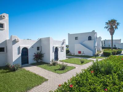 Weiß getünchte Ferienhäuser mit Garten und Palmen unter klarem blauem Himmel