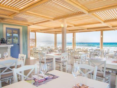 Helles, offenes Restaurant mit weißen Möbeln und Meerblick unter einem Holzlamellendach.