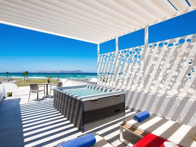 Strandterrasse mit Pool, Liegestühlen und Meerblick bei klarem Himmel und Sonnenschein.