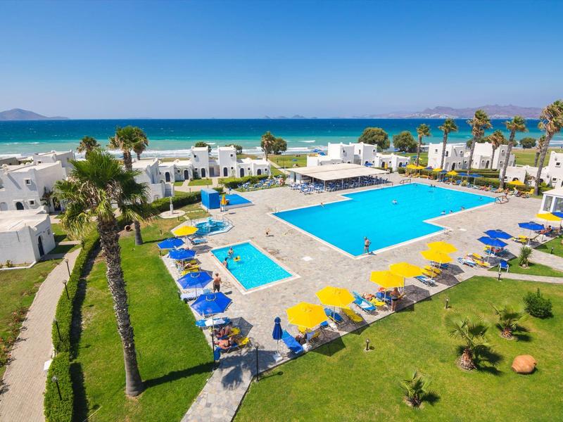 Hotelanlage mit großem Swimmingpool, Liegestühlen und weißen Bungalows am Strand.