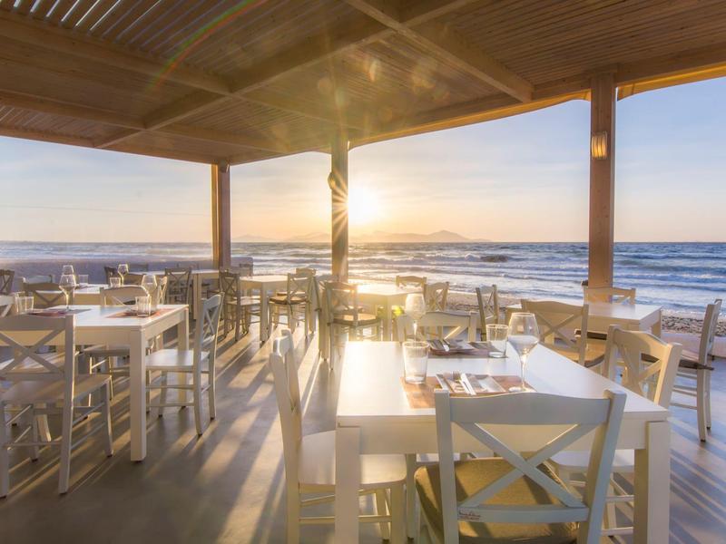 Offenes Restaurant am Meer mit weißen Tischen und Stühlen bei Sonnenuntergang