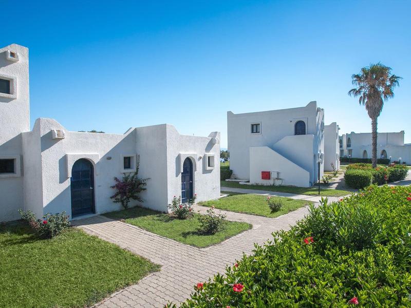 Weiß getünchte Ferienhäuser mit Garten und Palmen unter klarem blauem Himmel