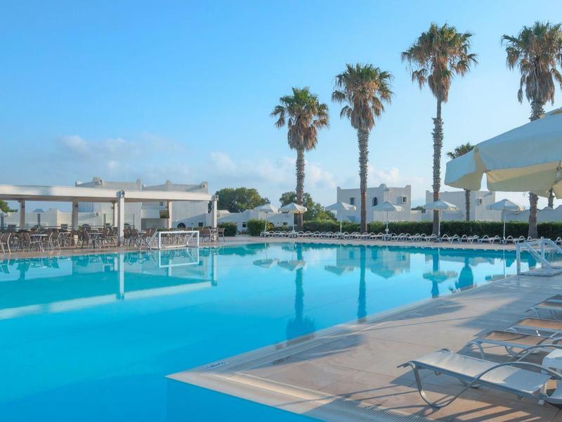 Großer Poolbereich mit Liegestühlen, Sonnenschirmen und Palmen unter klarem Himmel.