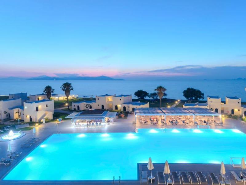 Großer beleuchteter Pool mit Palmen und Meerblick in einer Luxushotelanlage bei Sonnenuntergang