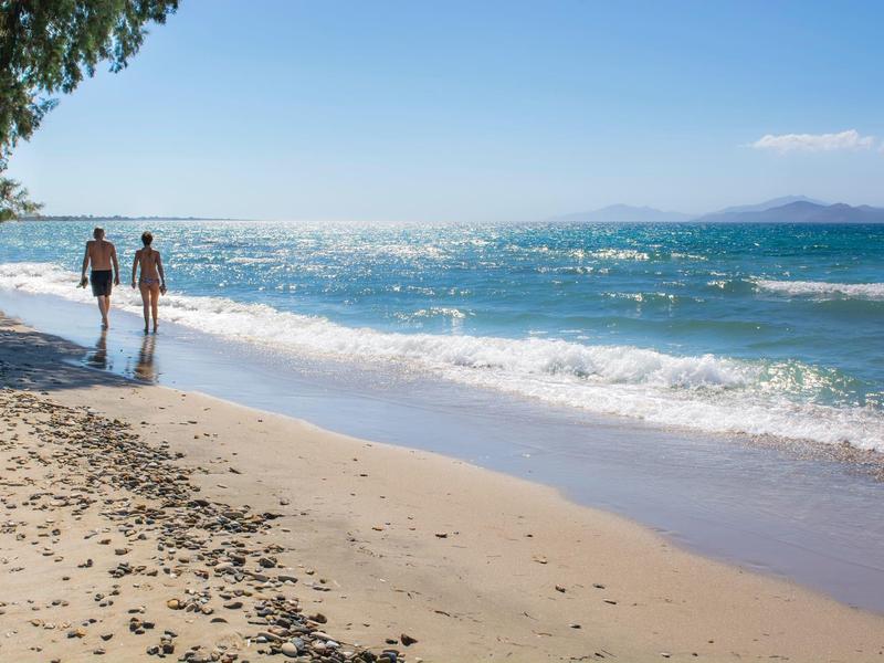 Paar spaziert am sonnigen Sandstrand entlang mit blauem Himmel und ruhigem Meer.