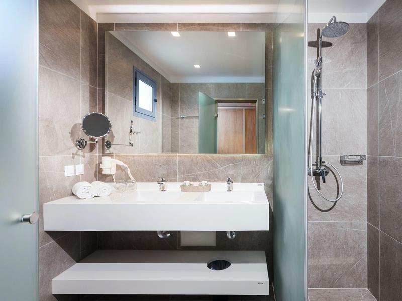 Modernes Hotelbadezimmer mit Waschbecken, großem Spiegel und Regenwalddusche.