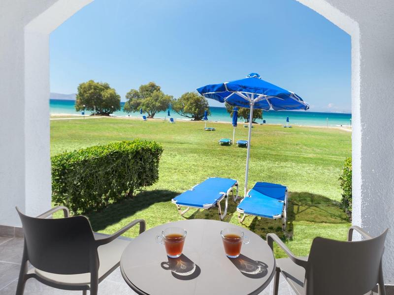 Blick durch einen Bogen auf Terrasse mit Tisch, zwei Stühlen und Kaffee, dahinter Rasen und Strand