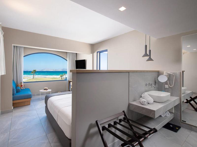 Hell eingerichtetes Schlafzimmer mit Meerblick, Doppelbett, Sitzecke und moderner Badezimmereinrichtung.