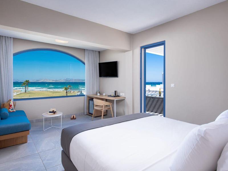 Helles Hotelzimmer mit Doppelbett, Sofa, Schreibtisch, Meerblick und Zugang zu einem Balkon.