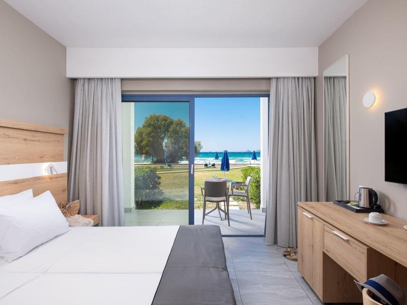 Hotelzimmer mit Doppelbett, Schreibtisch und Blick auf Terrasse mit Meerblick.