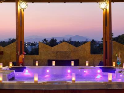 Vasca idromassaggio esterna illuminata al tramonto con vista su alberi e montagne.