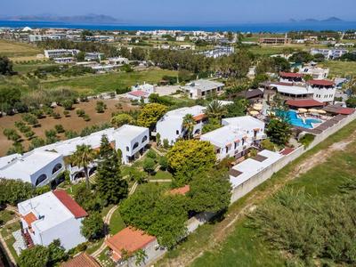 Widok z lotu ptaka na duży biały ośrodek z basenami i ogrodami blisko wody.