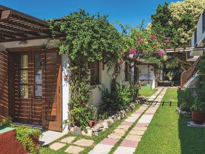 Giardino con erba verde e sentieri tra piccoli bungalow d'hotel imbiancati.