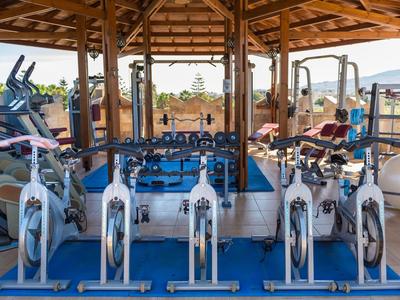 Diversi attrezzi da palestra e biciclette sotto un tetto di legno su un ponte aperto.