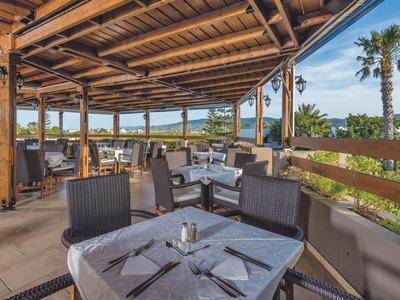 Überdachte Terrassenrestaurant mit gedeckten Tischen, Stühlen und Blick auf Palmen und Himmel.