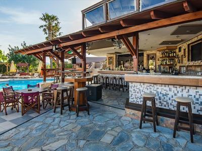 Bar all'aperto con sgabelli e posti a sedere accanto a una piscina in un ambiente tropicale.