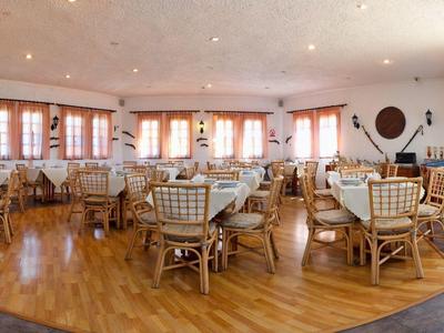 Przestronna jadalnia z drewnianą podłogą, wiklinowymi krzesłami i stołami przy dużych oknach.