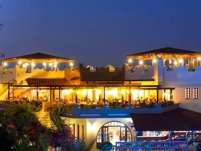 Oświetlony budynek hotelu o zmierzchu z zewnętrznym patio i ciepłym światłem.