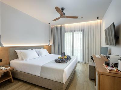 Jasny, nowoczesny pokój hotelowy z podwójnym łóżkiem, drewnianymi meblami, wentylatorem sufitowym i telewizorem.