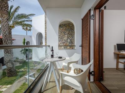 Balkon z białymi krzesłami i małym stolikiem z widokiem na ogród z palmami.