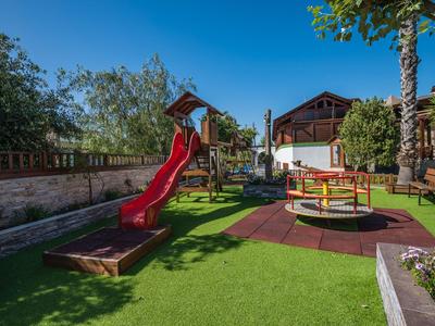 Parco giochi per bambini con scivolo e giostra in un giardino sotto un cielo limpido.