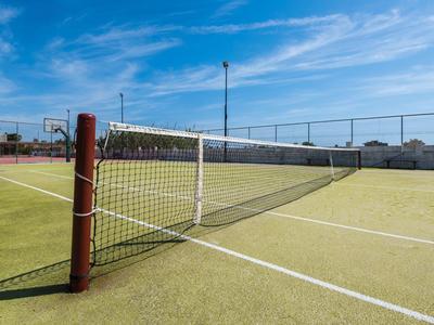 Campo da tennis con superficie verde e cielo blu sullo sfondo.