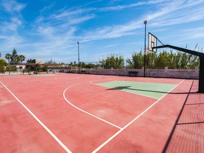 Campo da basket all'aperto con superficie rossa e cielo blu sullo sfondo.