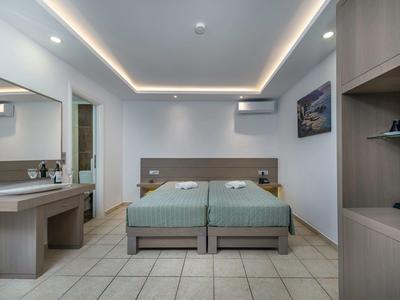 Nowoczesny pokój hotelowy z dwoma pojedynczymi łóżkami, stolikami nocnymi, toaletką i kafelkową podłogą.