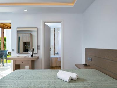 Nowoczesny pokój hotelowy z łóżkiem, zieloną narzutą, drewnianym biurkiem i otwartymi drzwiami do łazienki.